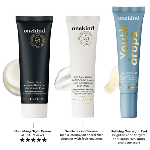 Three skin care products from onekind, including a dark blue tube of Dream Cream Nighttime Moisturizer, a white tube with gold and black writing of Clean Slate Barrier Boosting Facial Cleanser, and a light blue tube of Youthdrops Gentle Refining Peel serum.
