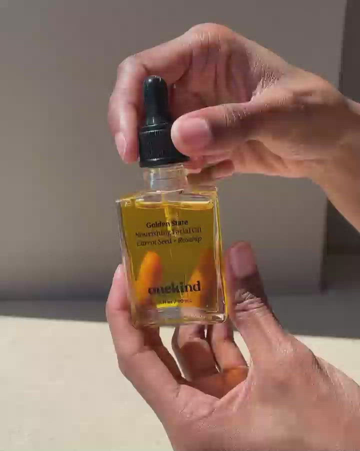A video with two hands holding the Golden State Nourishing Facial Oil in a clear jar that shows the golden oil with a black dropper top. One hand unscrews the lid and lifts it, allowing the oil to drip into the jar, and then lows the dropper and screws it back on.